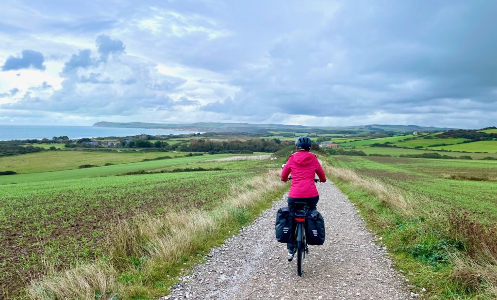 cycliste de dos sur chemin caillouteux en descente avec vue sur la côte direction Wissant.
